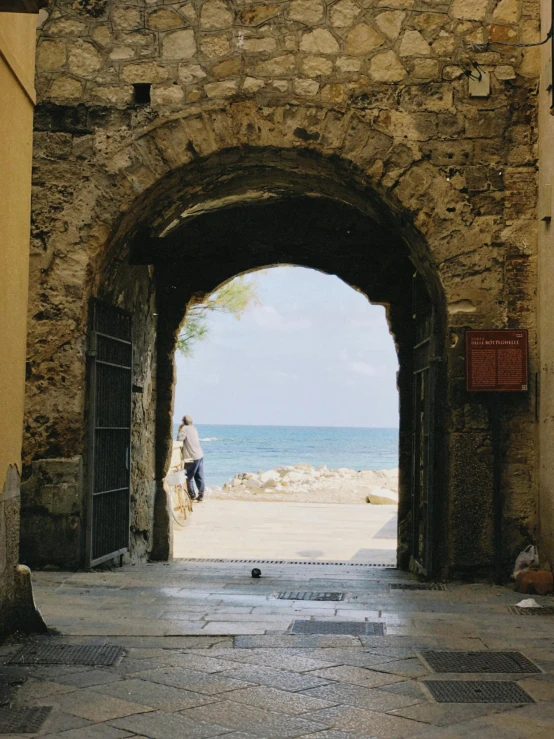 a person walking into a small archway to the ocean