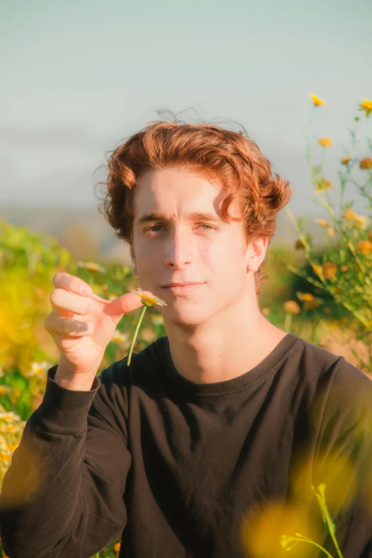 a young man is sitting on a field and eating flowers