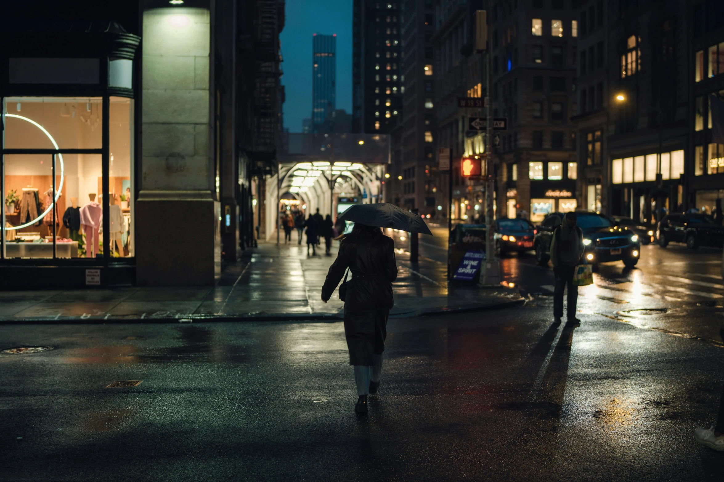 a street at night with people walking across the street with umbrellas