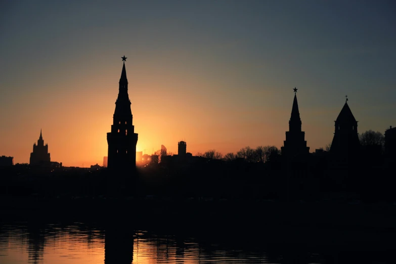 the sun rising behind some tall buildings with spires