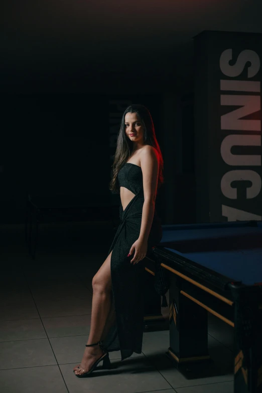 a woman in a black dress posing next to a pool table