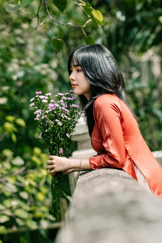 a woman is holding flowers and standing near a tree