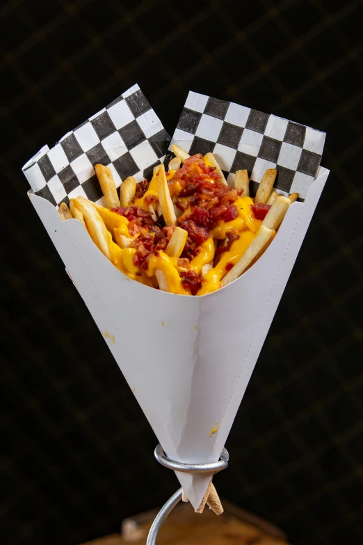 a cheesy potato and pepperoni chili cheese dog is in a paper cone