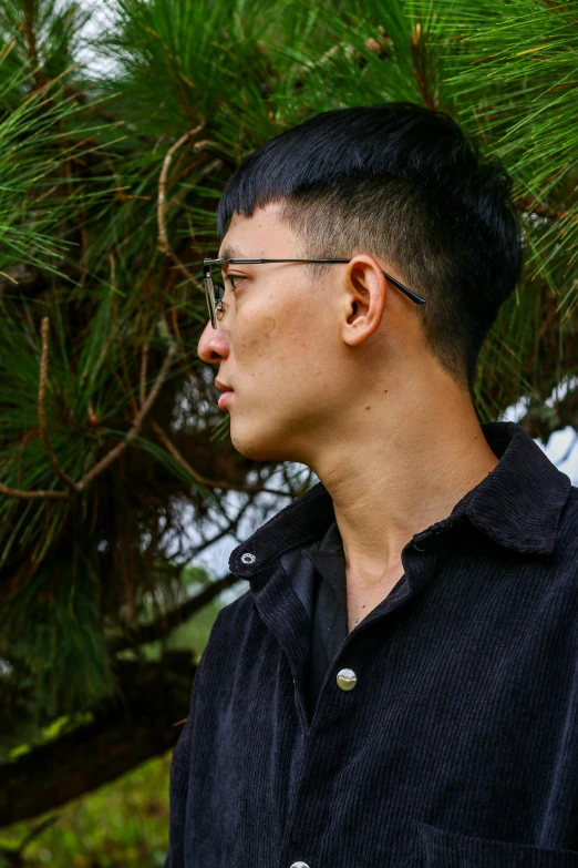 a man wearing glasses standing in front of a tree