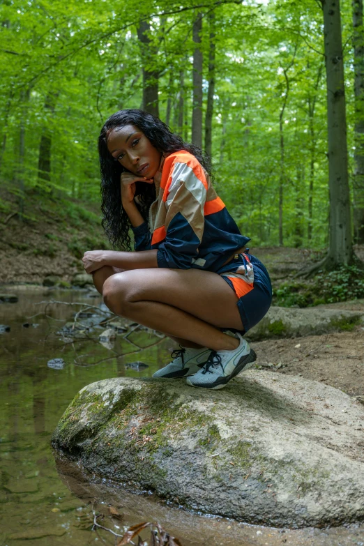 a girl squatting on a rock near a stream