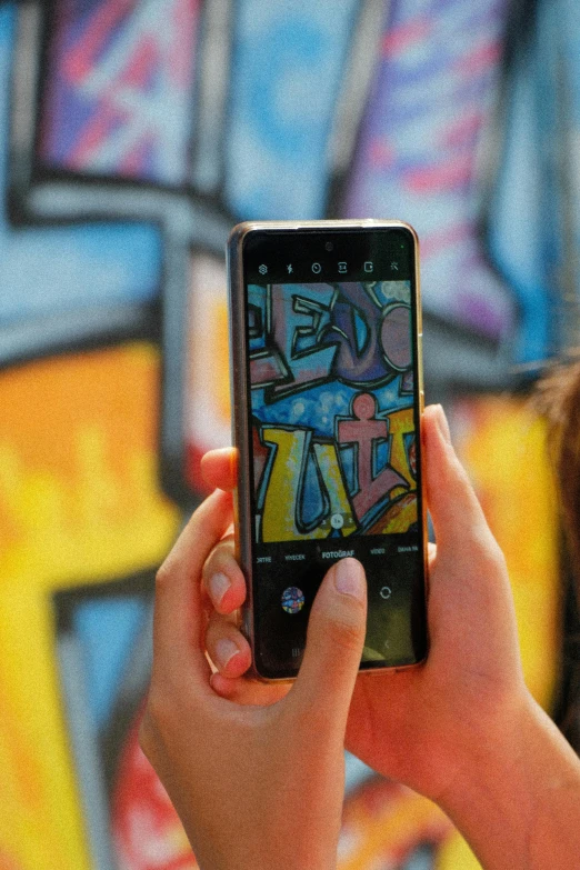 a hand holding a smart phone with graffiti in the background