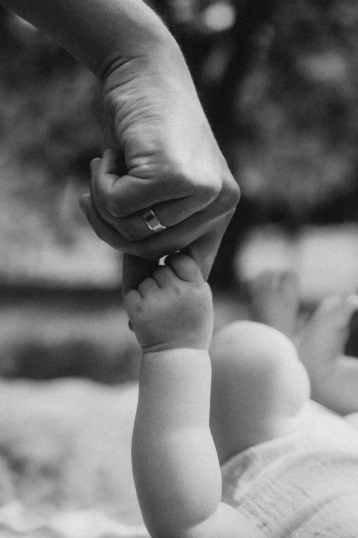 a black and white po of a baby's foot holding the hand of a hand