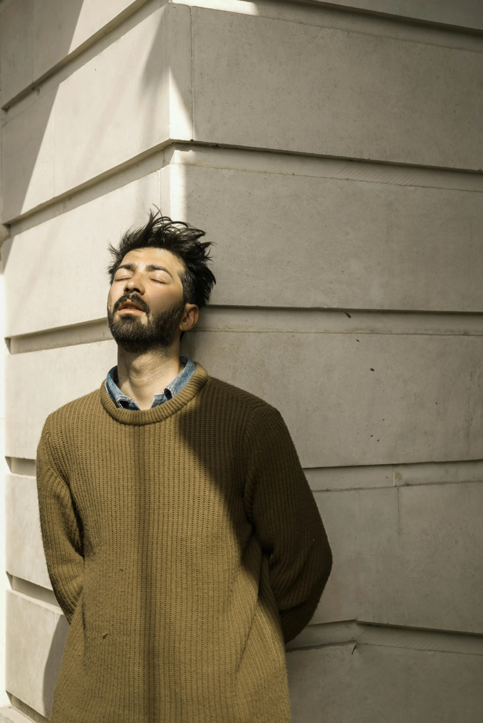 a bearded man leaning on the wall with his head on his hands