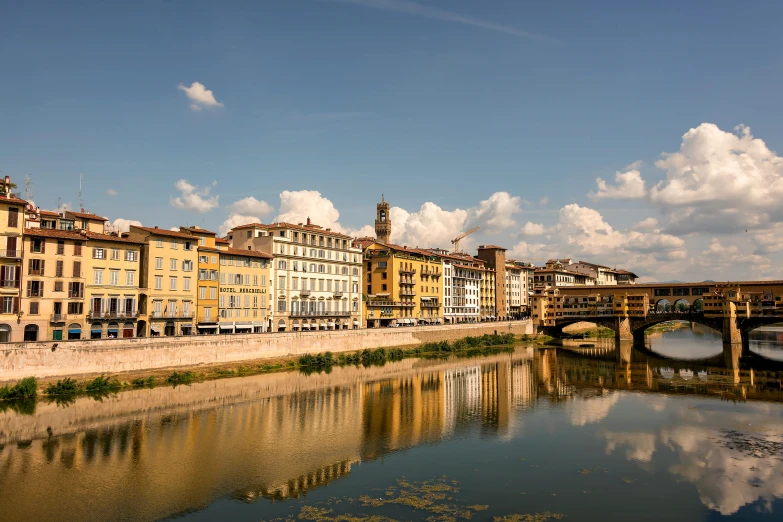 several buildings line the bank of the river with bridge in background