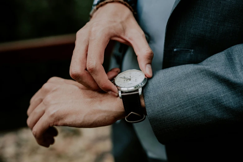 the man in a gray suit and brown celet holding his watch