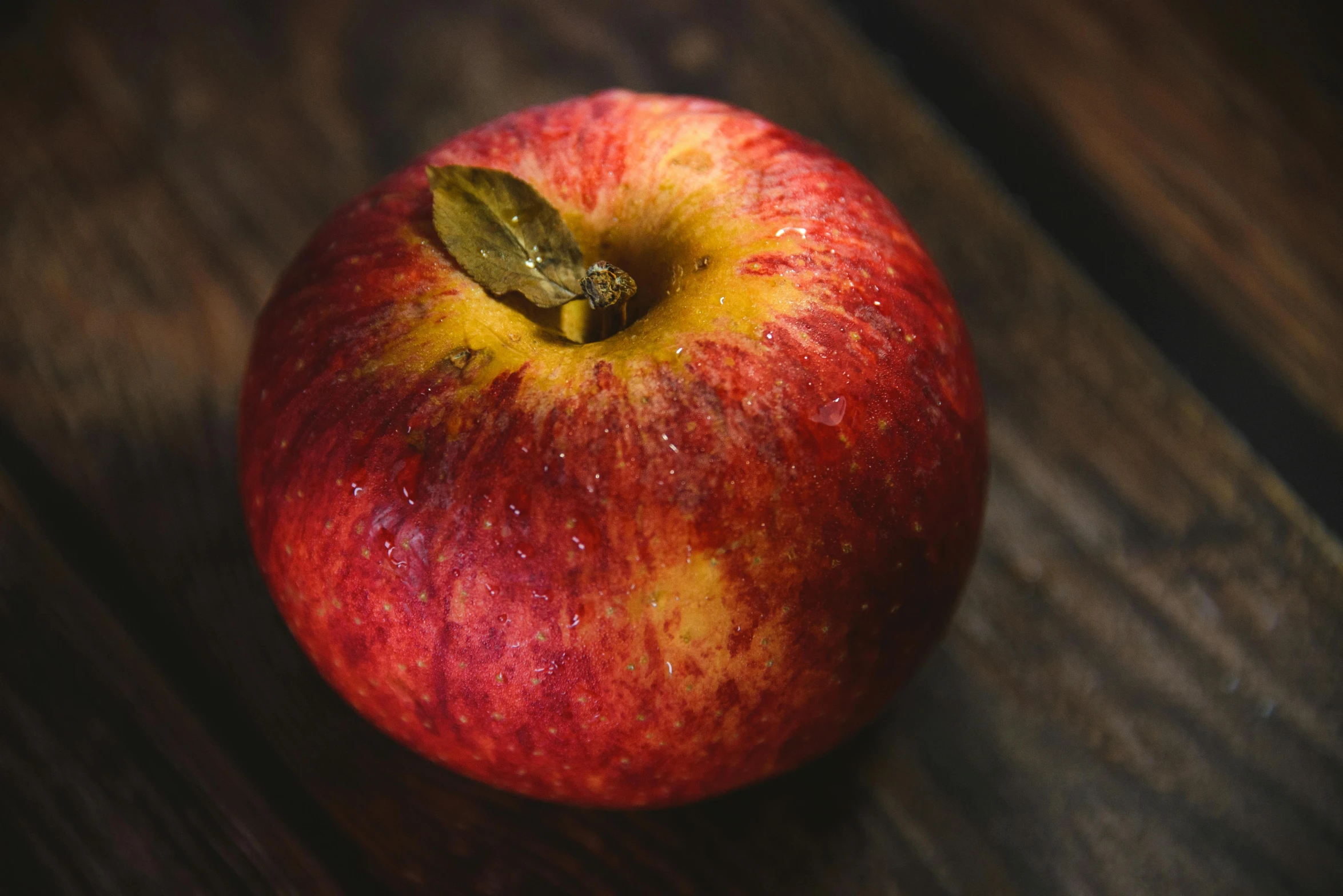 red apple with green leaves on wooden table