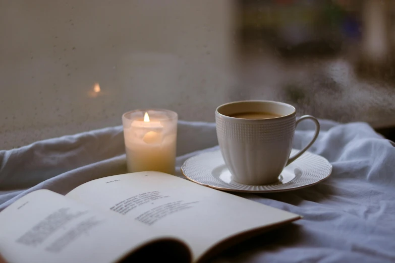 a tea cup with tea in it is next to an open book and lit candle