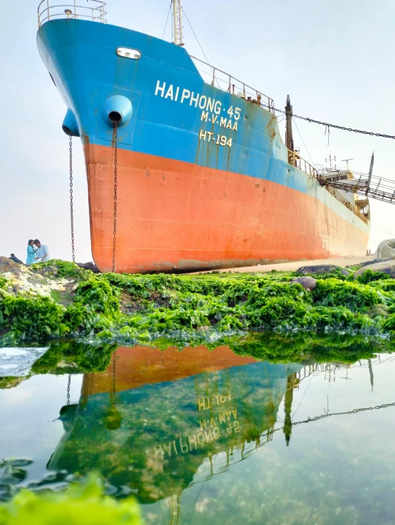 a large boat sits on land and is next to some water