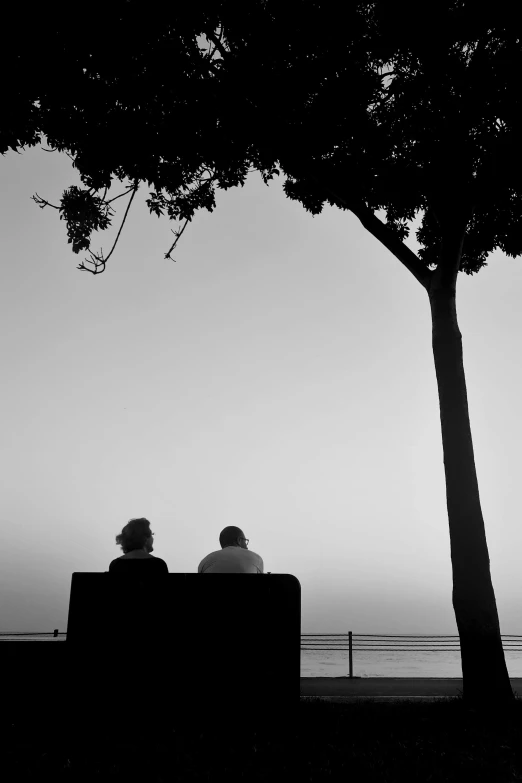 a black and white picture of a couple sitting on a bench