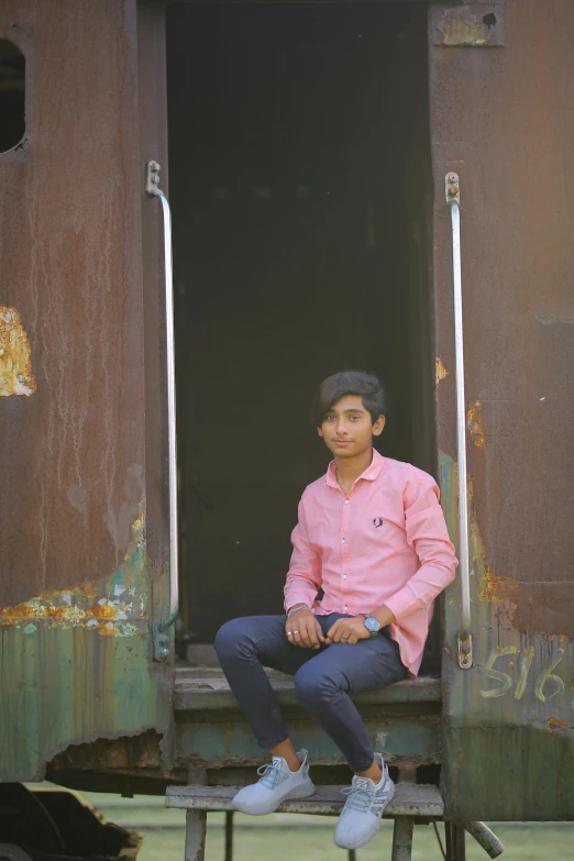 a man with dark hair sits on a piece of rusty metal and looks off into the distance