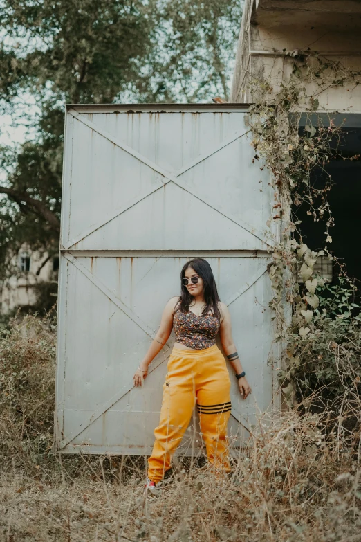 woman in sunglasses and yellow pants leaning on an old building