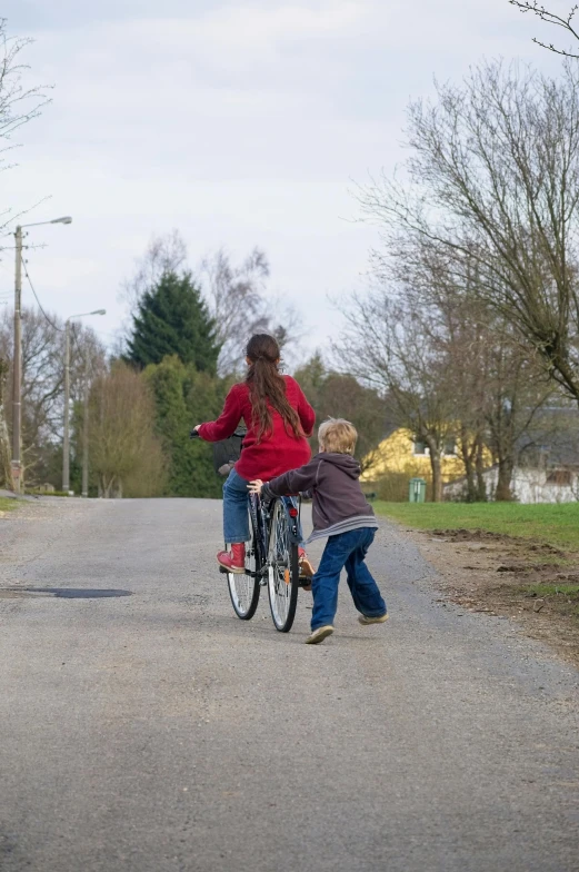 a woman and her child riding a bicycle on the side of the road