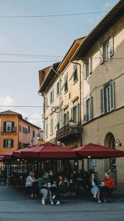 some people sit under umbrellas outside in front of buildings