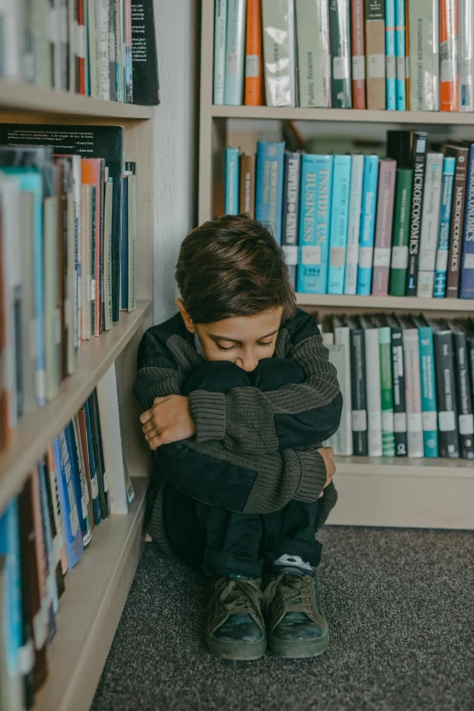 a  sitting on the floor in front of a book shelf with a bunch of books