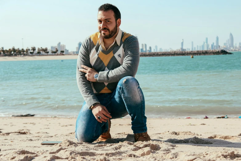 a man with a beard is kneeling on the sand next to the ocean