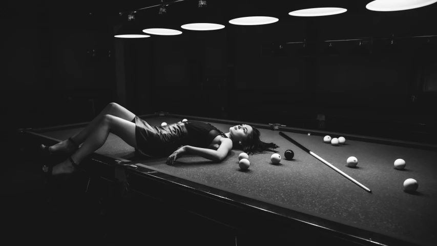 a woman lies on a pool table and balls lie around her