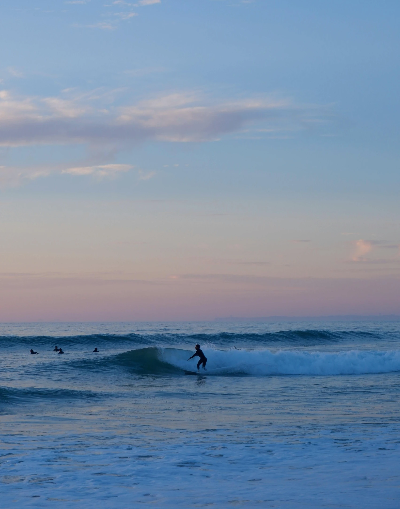 several people are in the ocean surfing at sunset