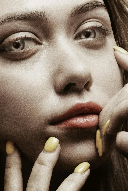 a woman wearing yellow nail polish and holding her hands near her face