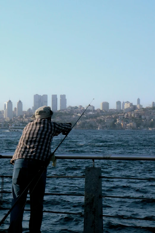 man fishing from a railing with the city in background
