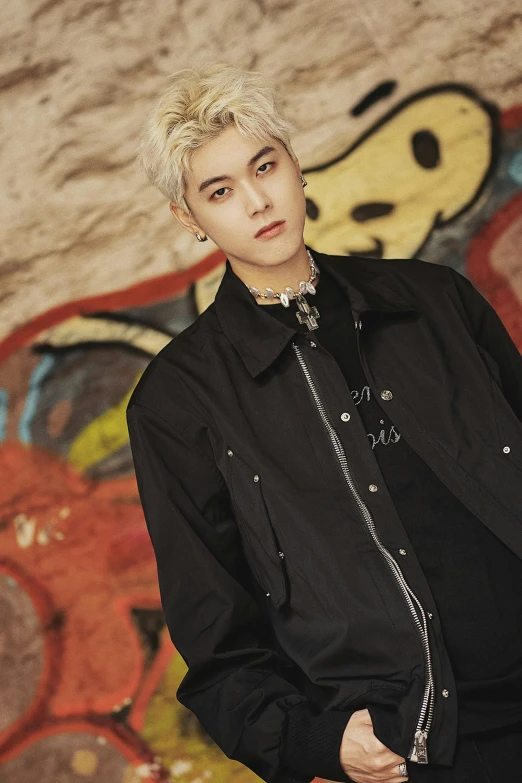 a male with blonde hair is posing in front of a wall