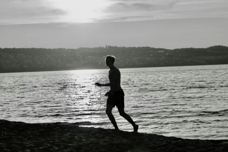 a man is walking next to the water with a frisbee