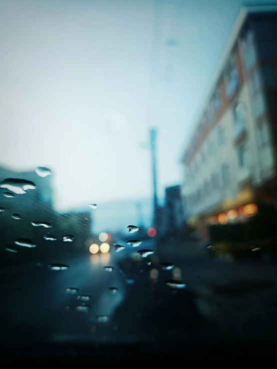 a close up of a rainy window with street cars and buildings
