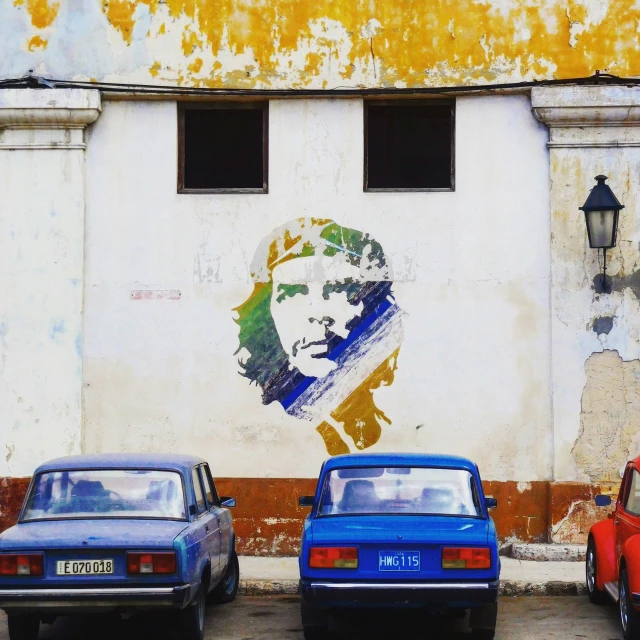 a wall painted with a picture of a president and 2 cars parked side by side