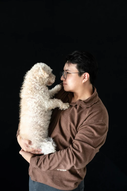 a young man holding a white poodle puppy in his right arm