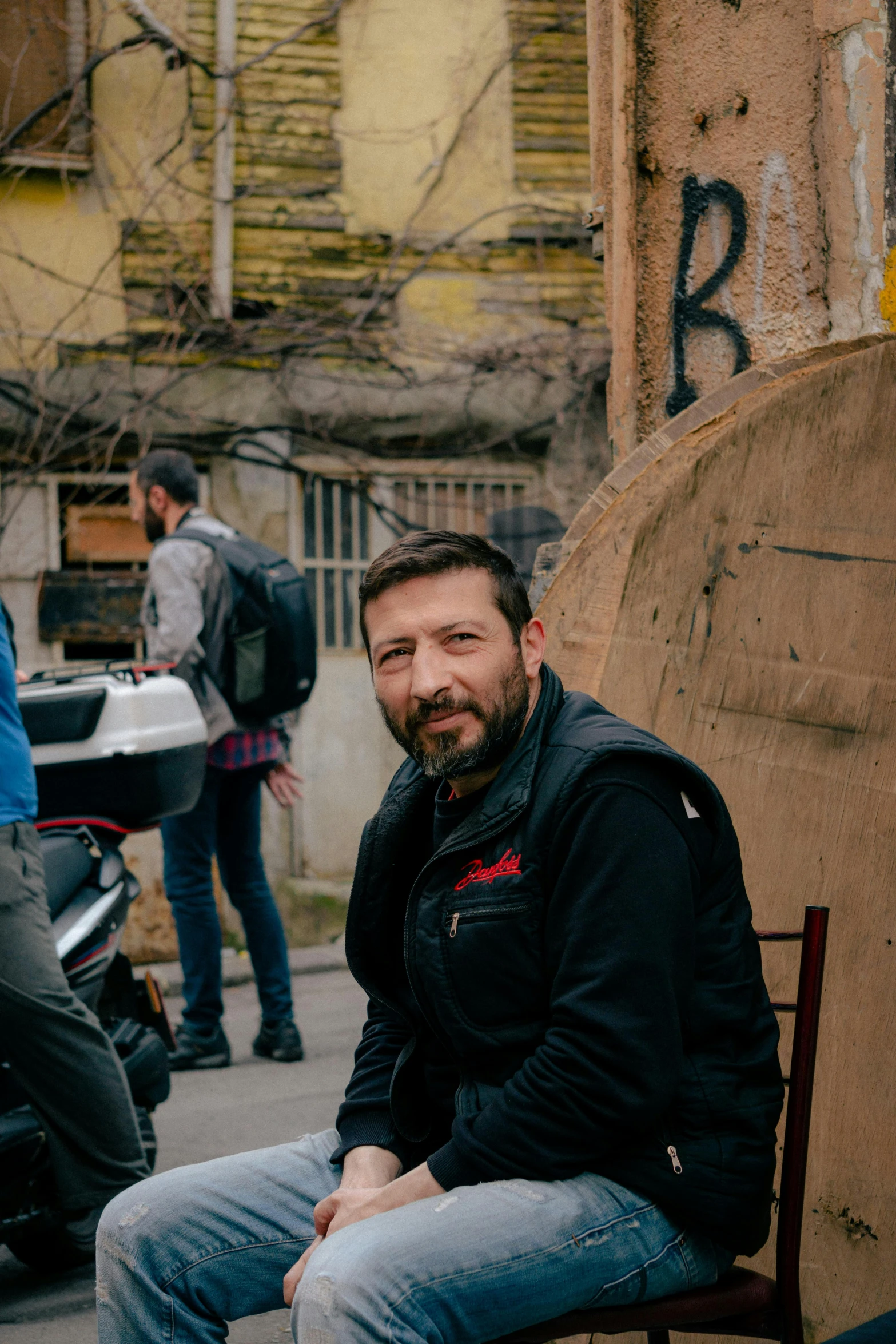 a smiling man sits next to his skateboard