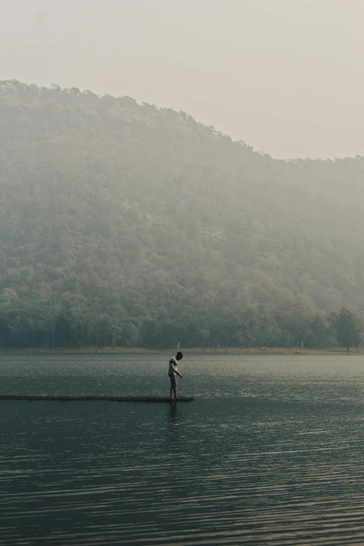 a man standing on a body of water holding a hat