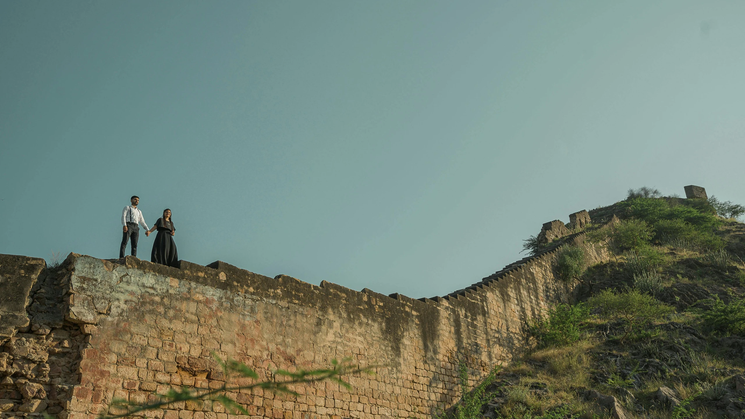 two people stand on top of a stone wall