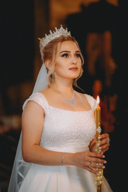 a woman in a white gown and tiara holding a lit candle