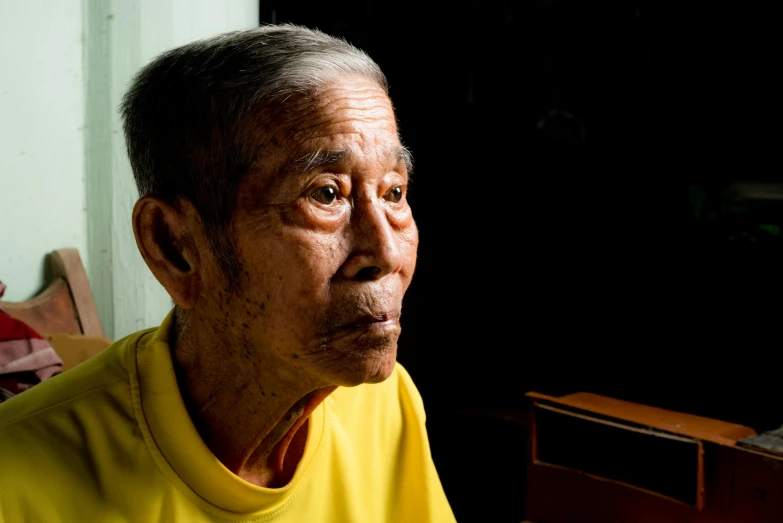 an older man sits in a dark room with furniture