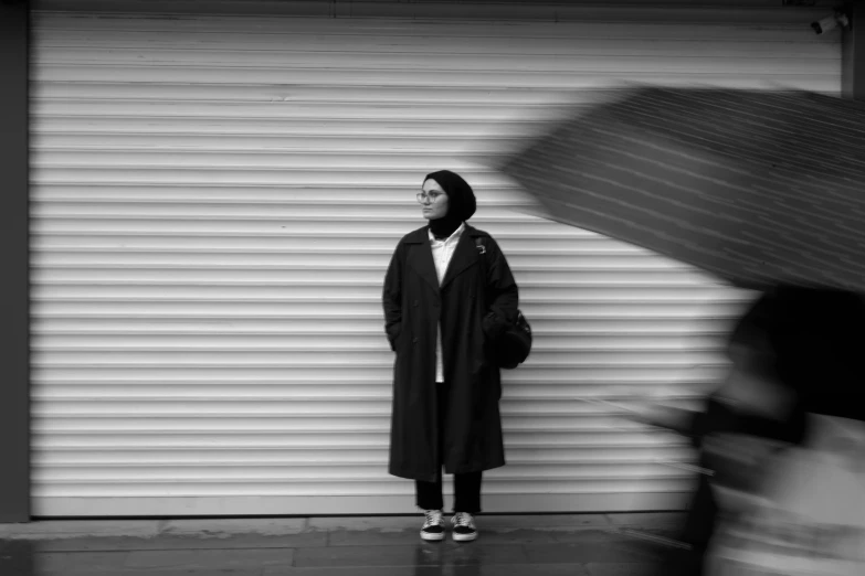 a woman in coat with umbrella next to building