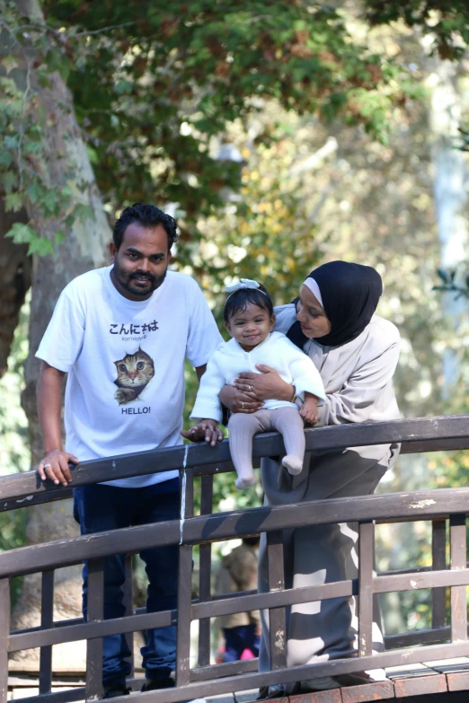 a man and woman standing on a bridge while holding a baby