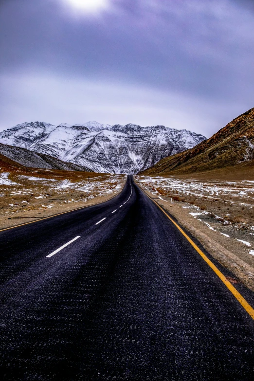 a long black road with a snow covered mountain in the distance