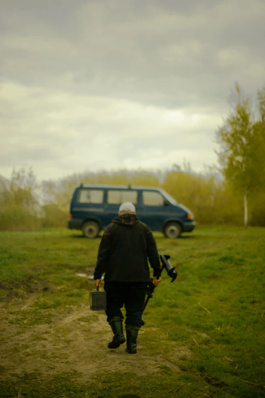 a man holding a guitar case on top of a lush green field