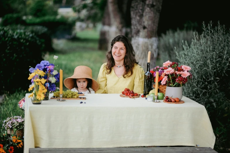 a woman and child sitting at a table with wine, flowers, fruit and candlelight candles