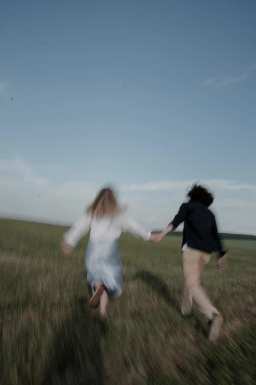 two people holding hands walking through an open field