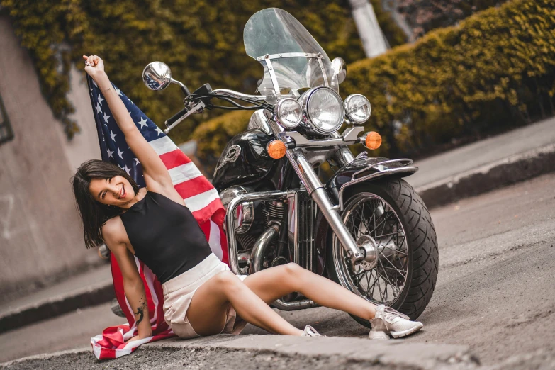 a young lady kneeling on the side of the street with her feet up and motorcycle in the background