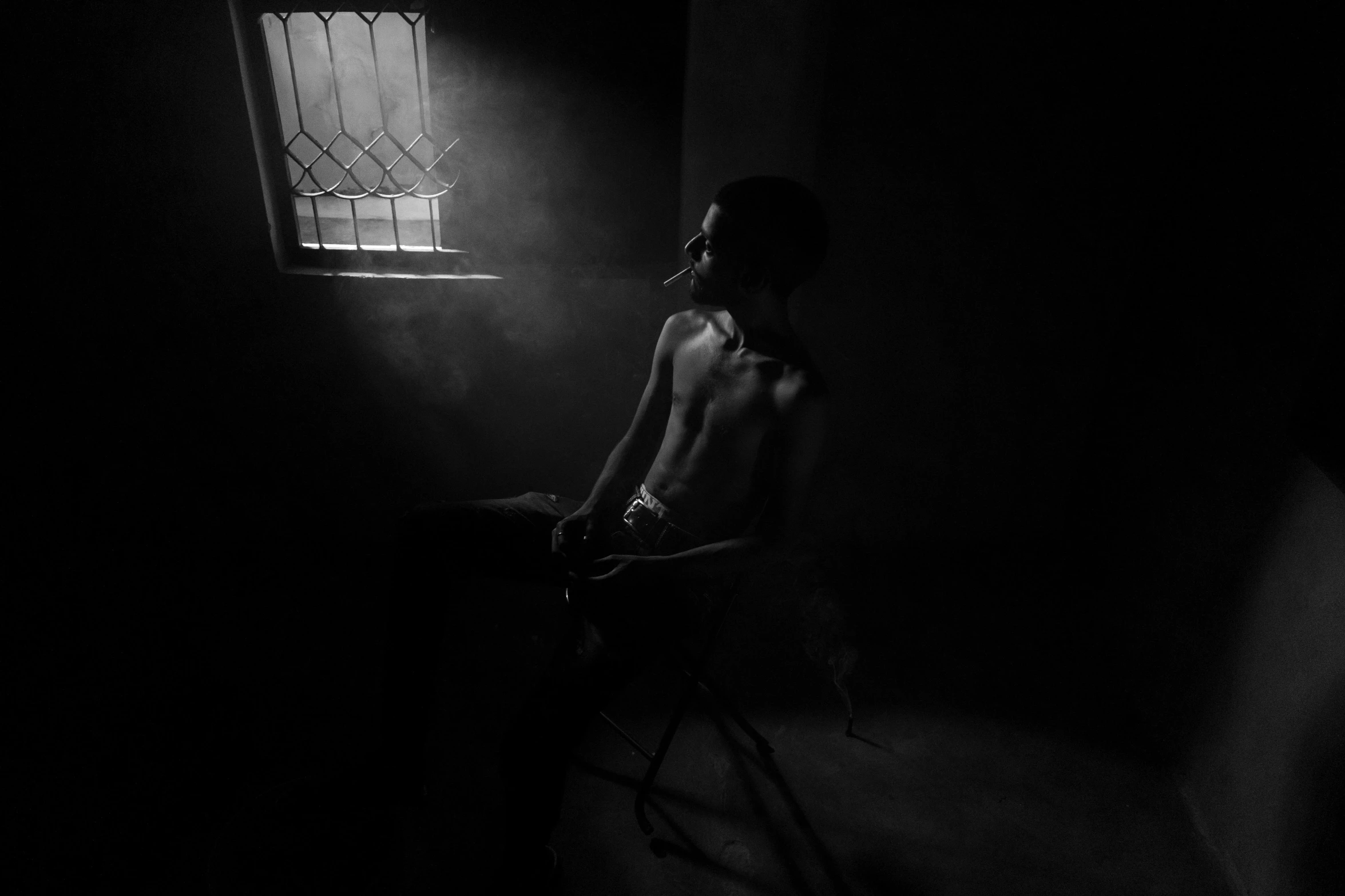 a man sitting on a chair in the dark looking out a window