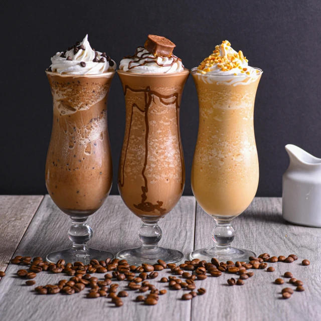 three milkshakes, with different flavors on a wooden surface