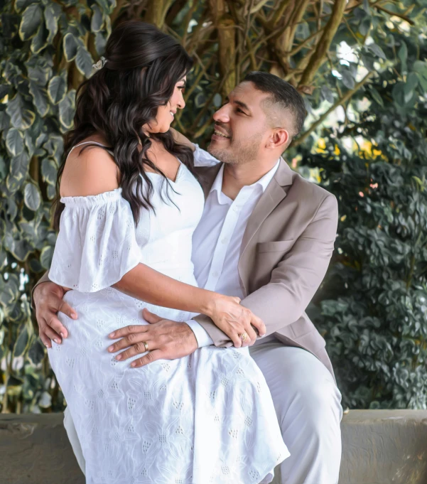 a couple cuddling close together in front of green plants