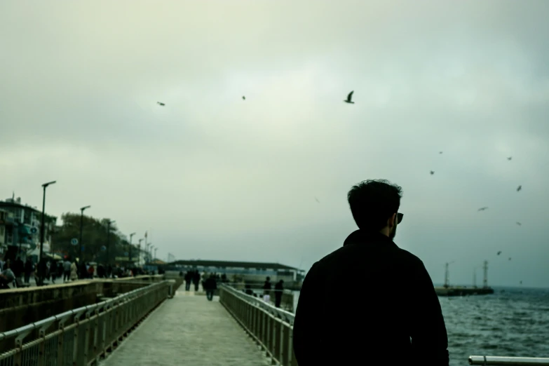 man looking at sea on cloudy day with birds flying in the sky