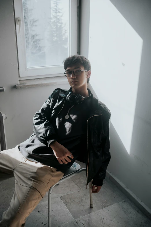 a young man wearing glasses sitting next to a window